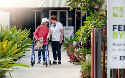 Aged care worker walking outside with senior lady with wheelie walker and puppy