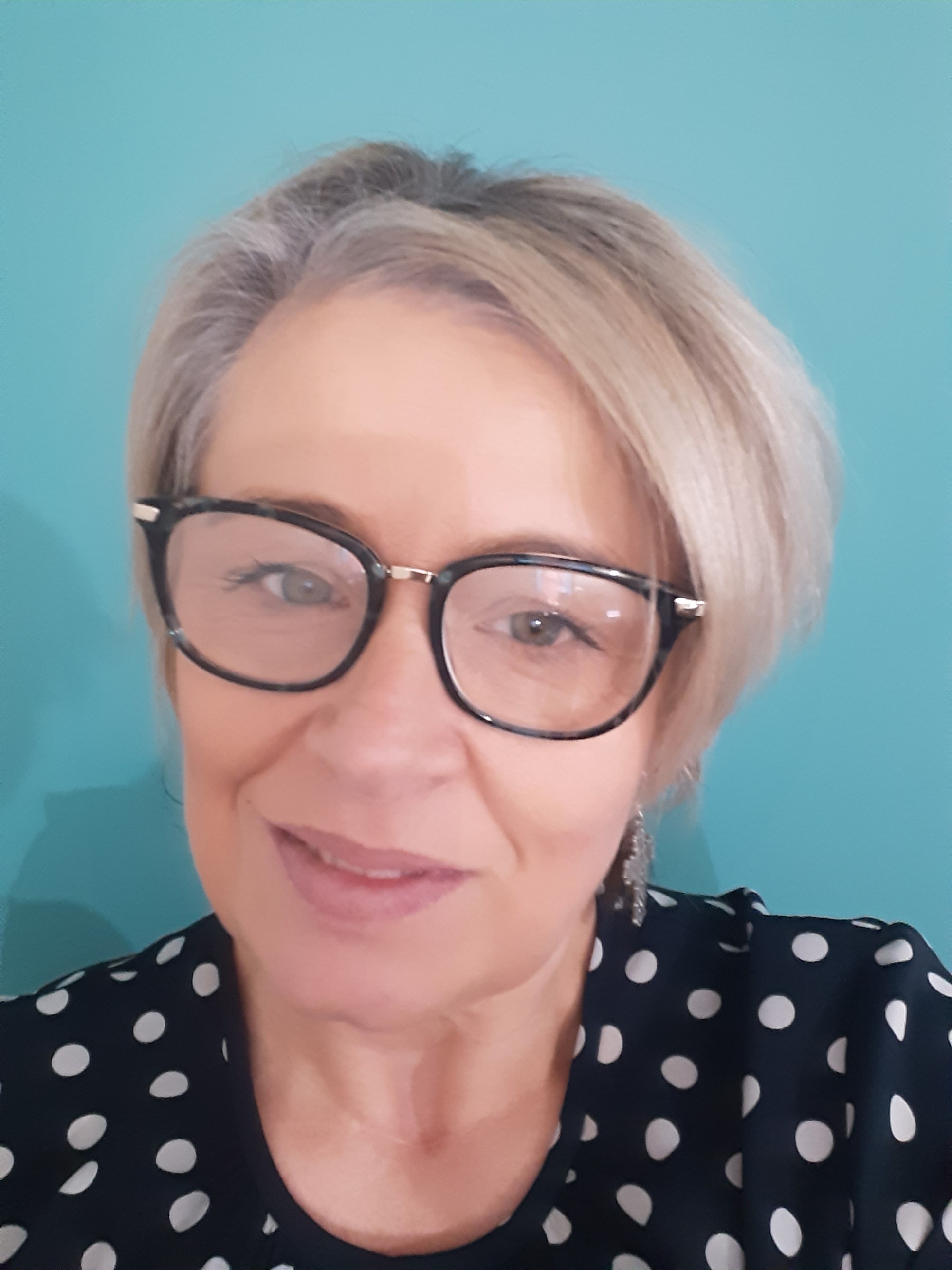 Selfie of middle-aged woman with glasses and bob cut in front of blue background