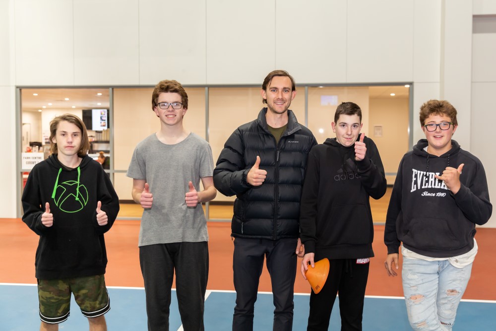 Young man with teenage boys giving thumbs up to camera in a sports hall