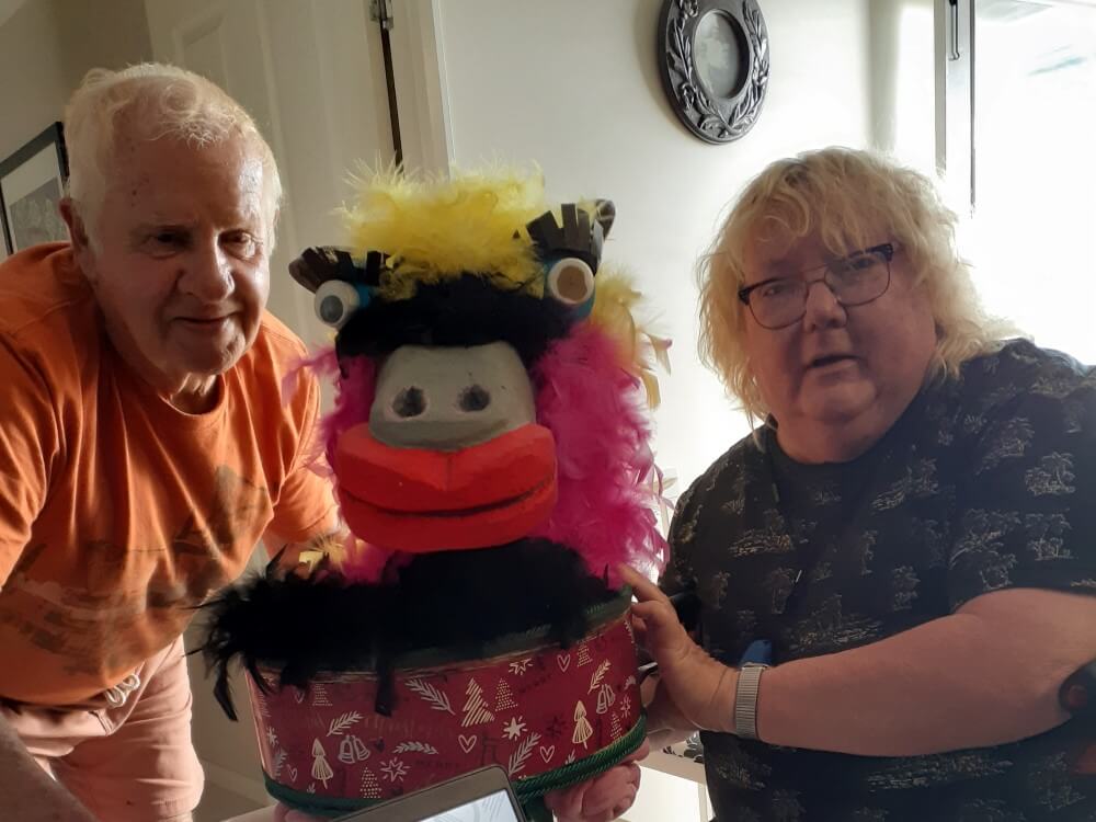 Two elderly men with a colourful, fun, craft-made hat