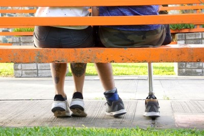 The feet of two people sitting close together on a branch, one able bodied, and one with a prosthetic leg