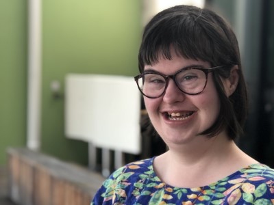 Girl with Down syndrome, short dark hair and glasses smiling at camera