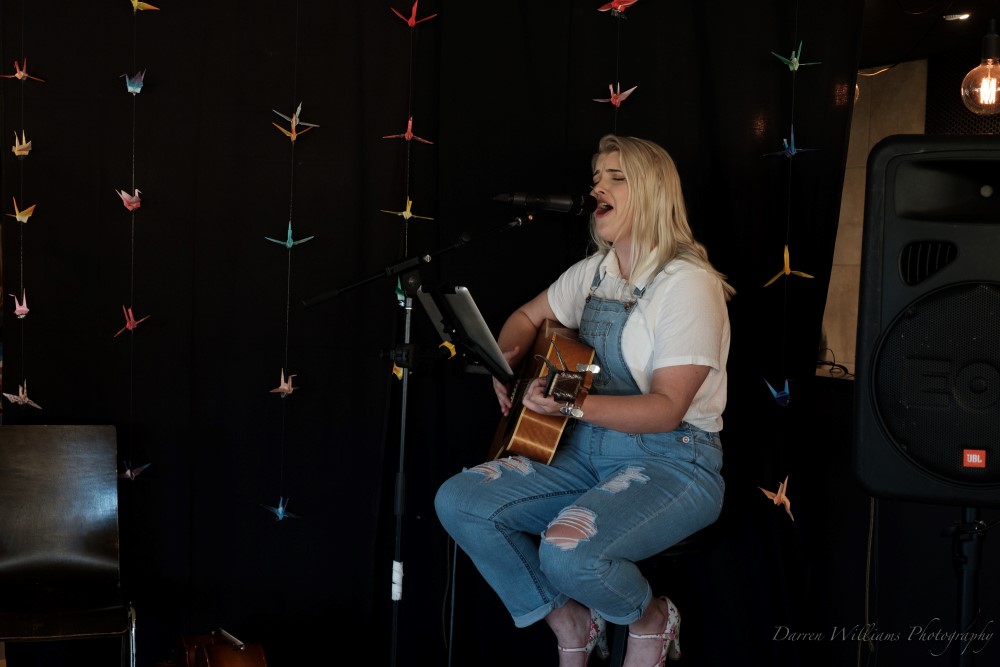 Young blonde woman sitting on stool, playing the guitar, and singing