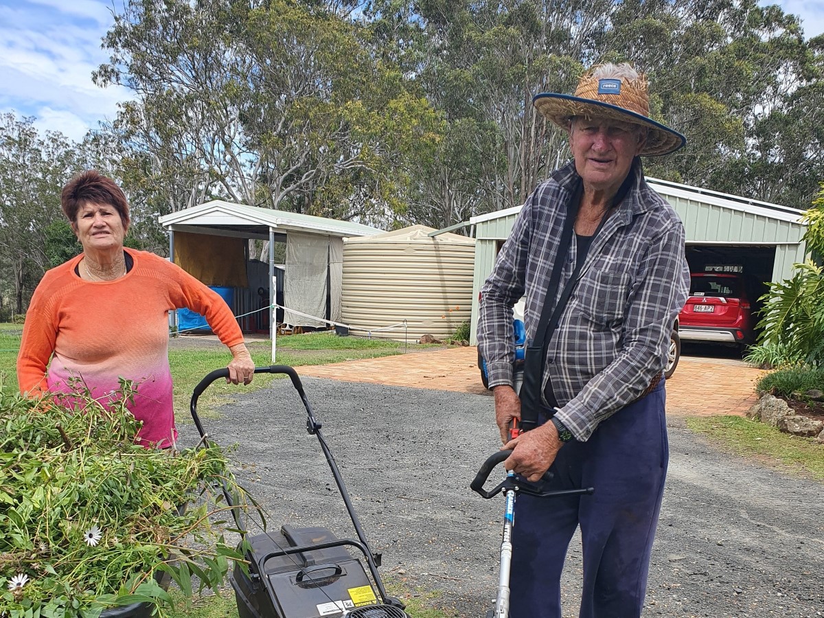 Senior lady holding onto lawn mower and senior man holding onto a whipper snipper in the garden