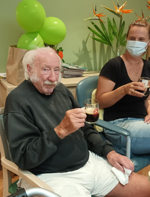 Senior man sitting down and drinking Guinness with green balloons behind him