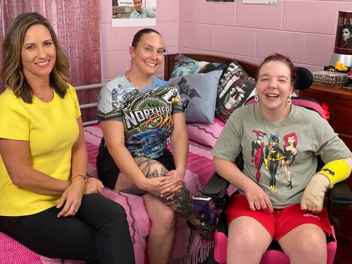 Two women sitting on a bed with a girl in a wheelchair next to them