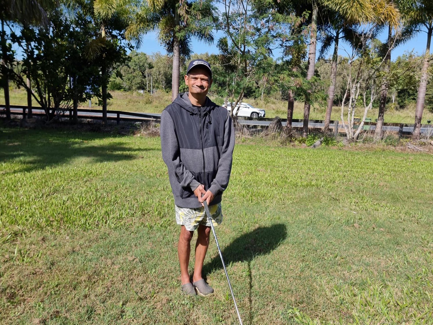 Man wearing large grey jumper standing in a gold course, holding a club