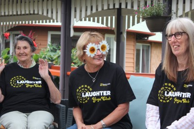 Three older women sitting in black Laughter Yoga T-shirts