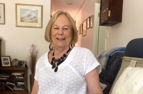 Older lady in white smiling at camera indoors