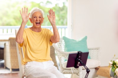 Senior lady in bright yellow T-shirt holding up both arms in front of a tablet