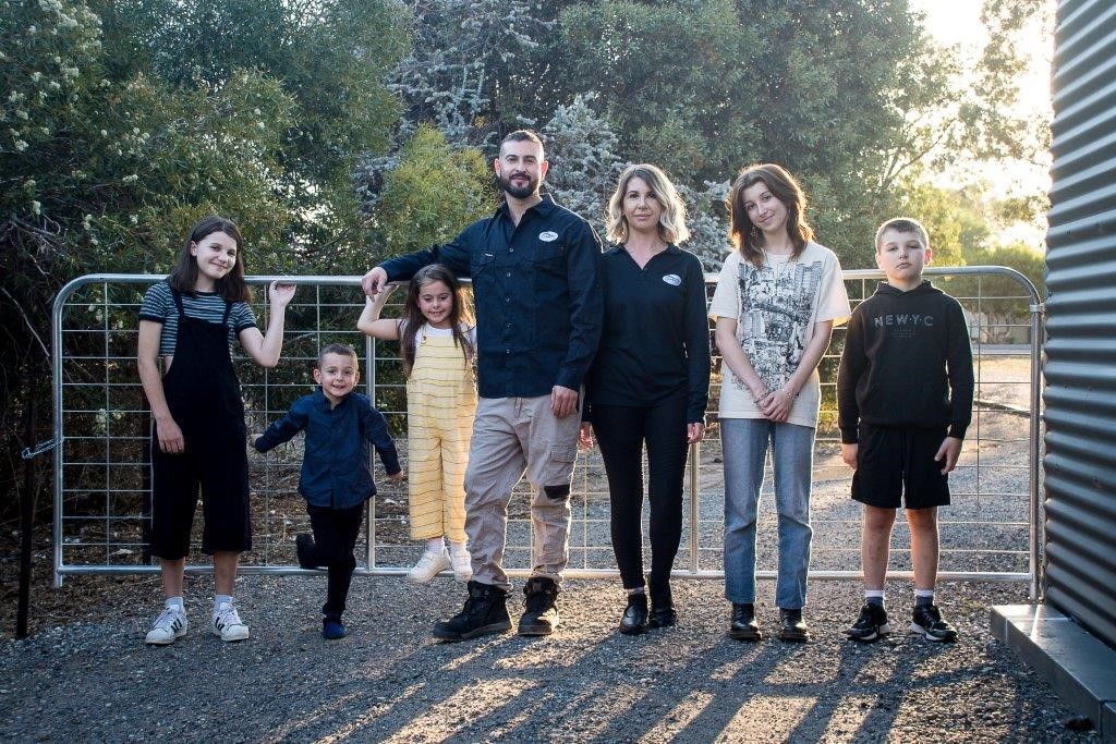 Family of seven posing outside along a fence