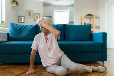 Senior lady in pink blouse on the floor in front of blue couch after having fallen