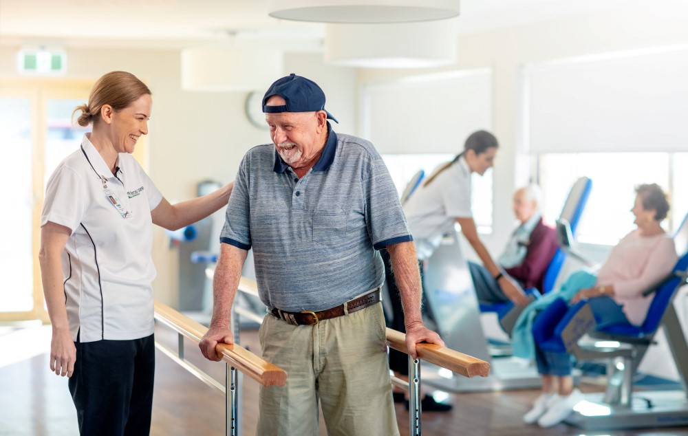 Senior man standing up with the help of young female physiotherapist