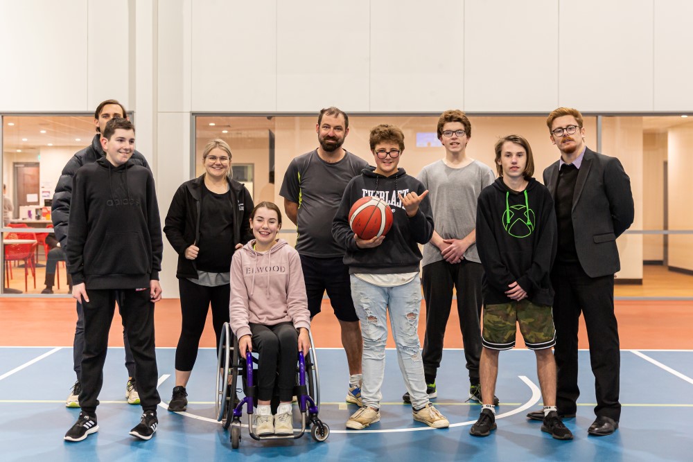 Team of adults, kids, and a girl in a wheelchair posing on a court with a basketball