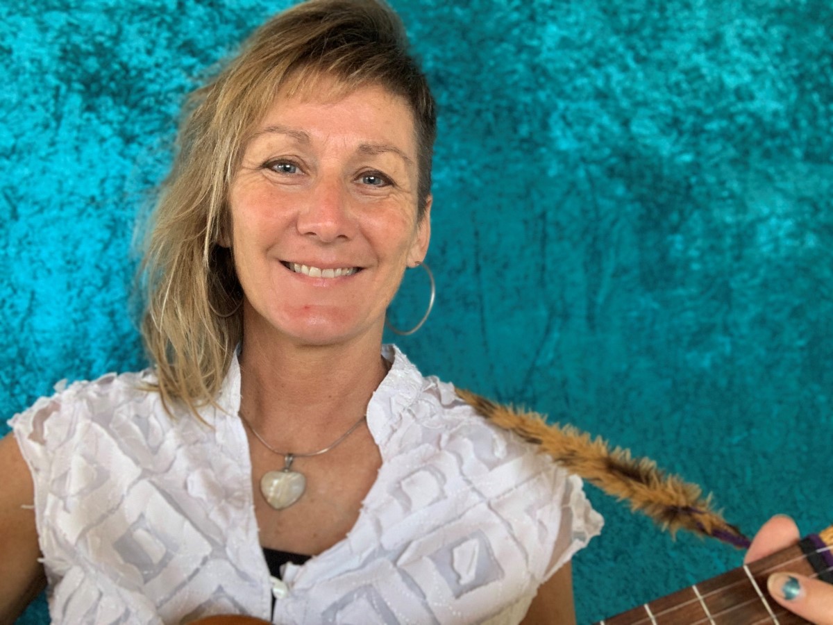 Blonde woman with her hair shaved on one side holding a guitar in front of a blue velvet background 