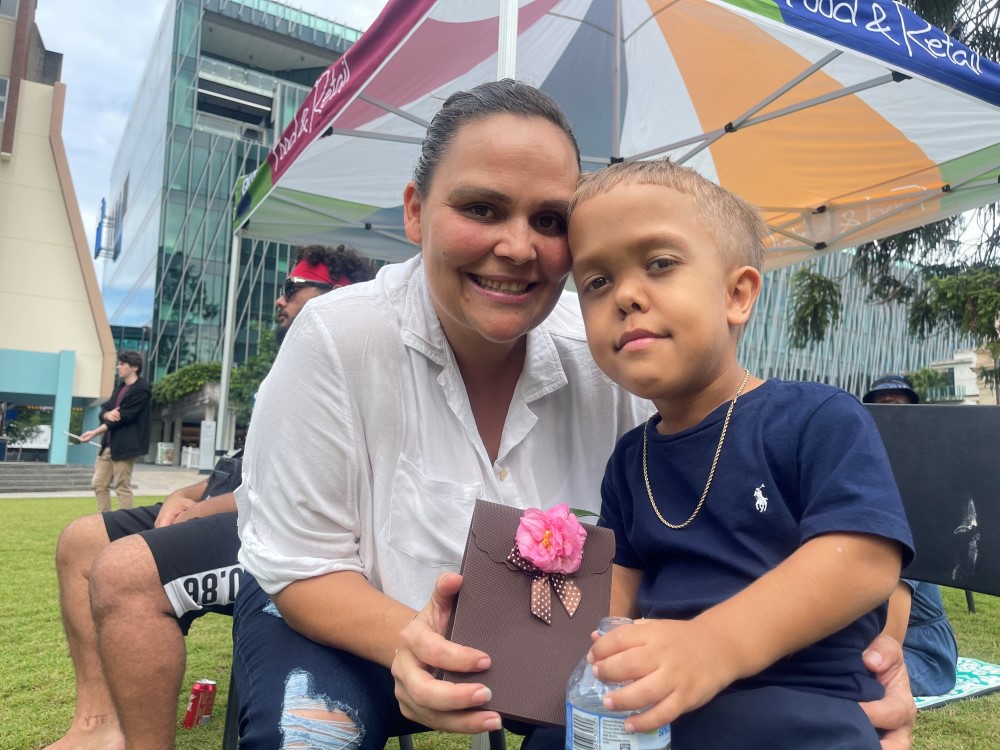 First Nations mother holding a gift bag with her child who has dwarfism 