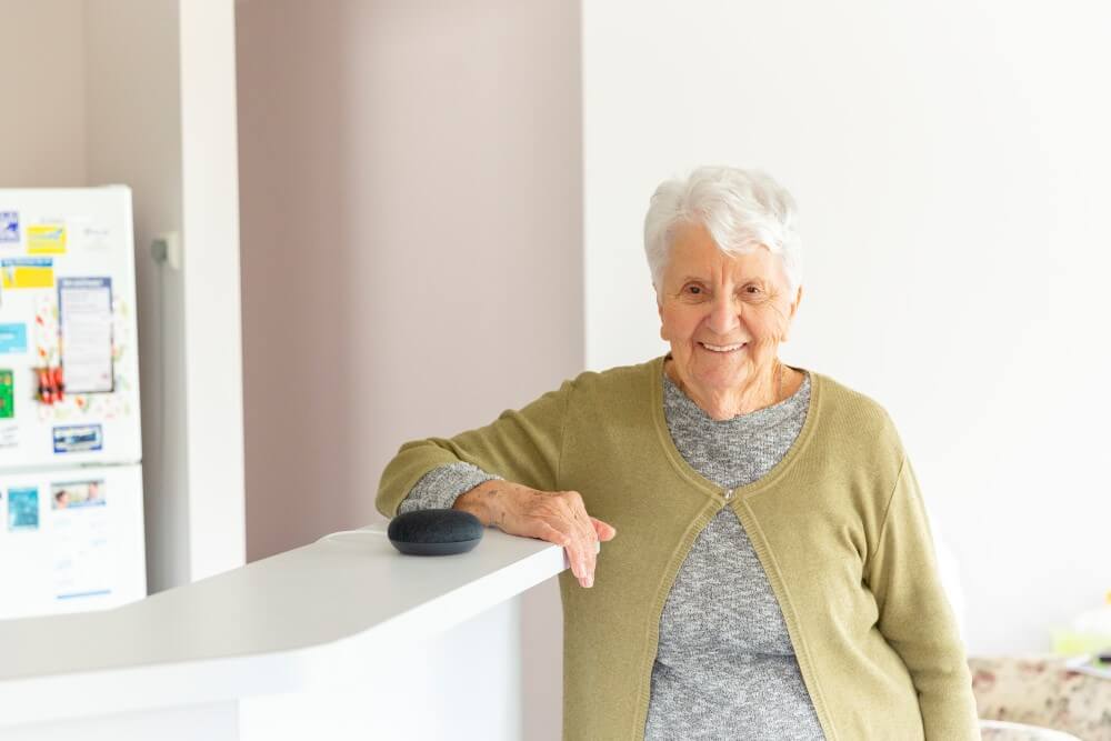 Elderly lady standing at counter with a Google Home device next to her