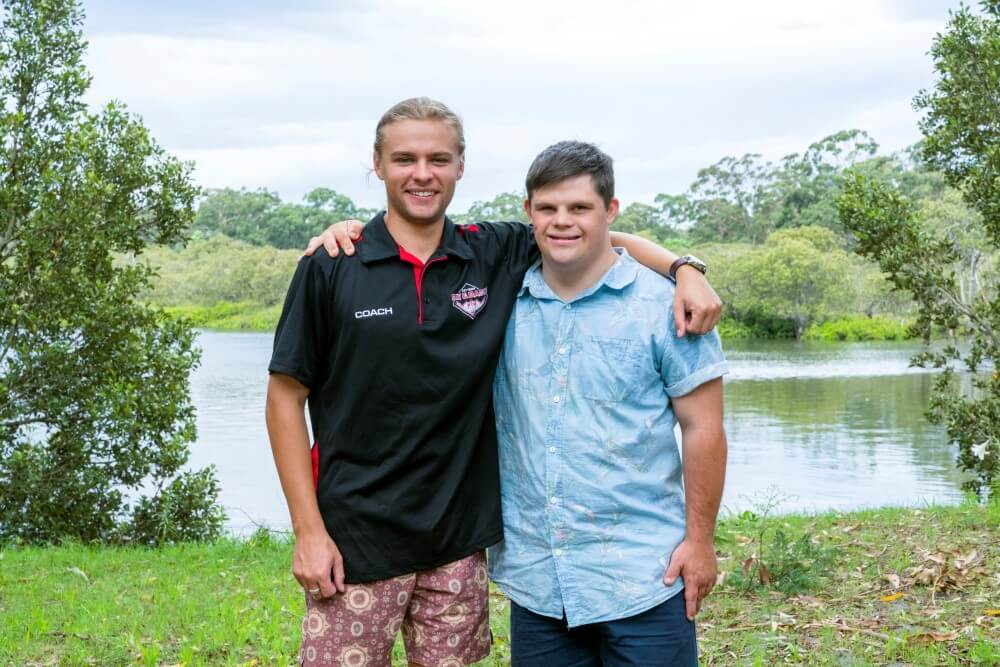 Two teenagers hugging and posing for the camera, one has Down syndrome