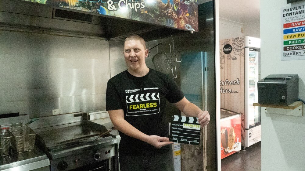 Man in a restaurant kitchen holding a clapboard 