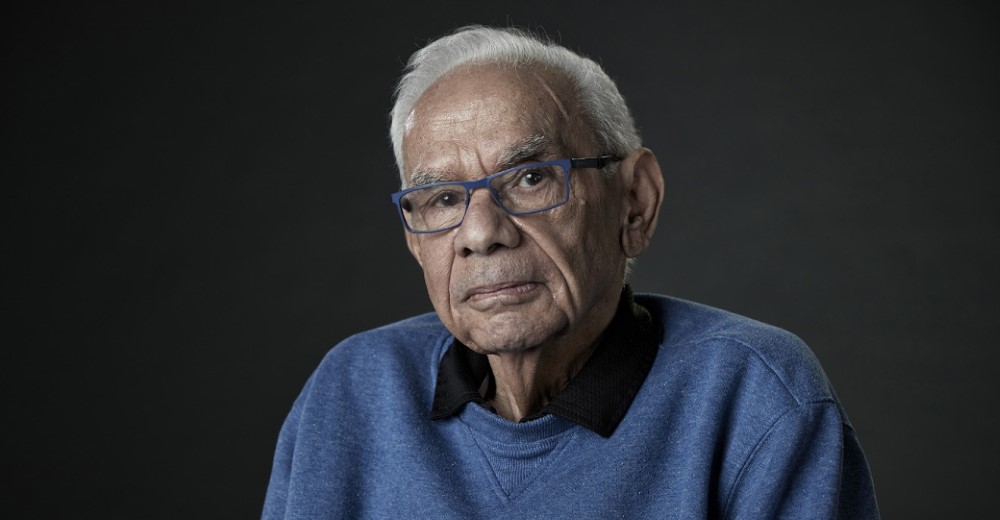 Elderly Aboriginal man posing for camera in front of black background 