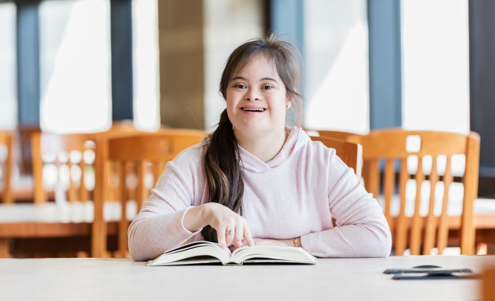 Smiling girl with Down Syndrome reading a text book