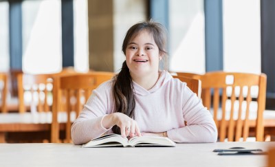 Smiling girl with Down Syndrome reading a text book