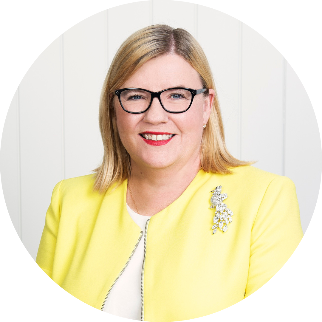 Blonde woman with dark framed glasses wearing bright red lipstick, a yellow top and a brooch