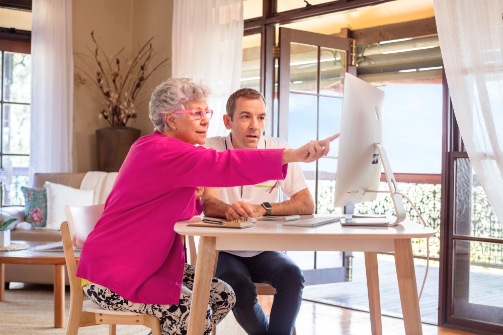 Lady with pink cardigan looking and pointing at computer with young man 