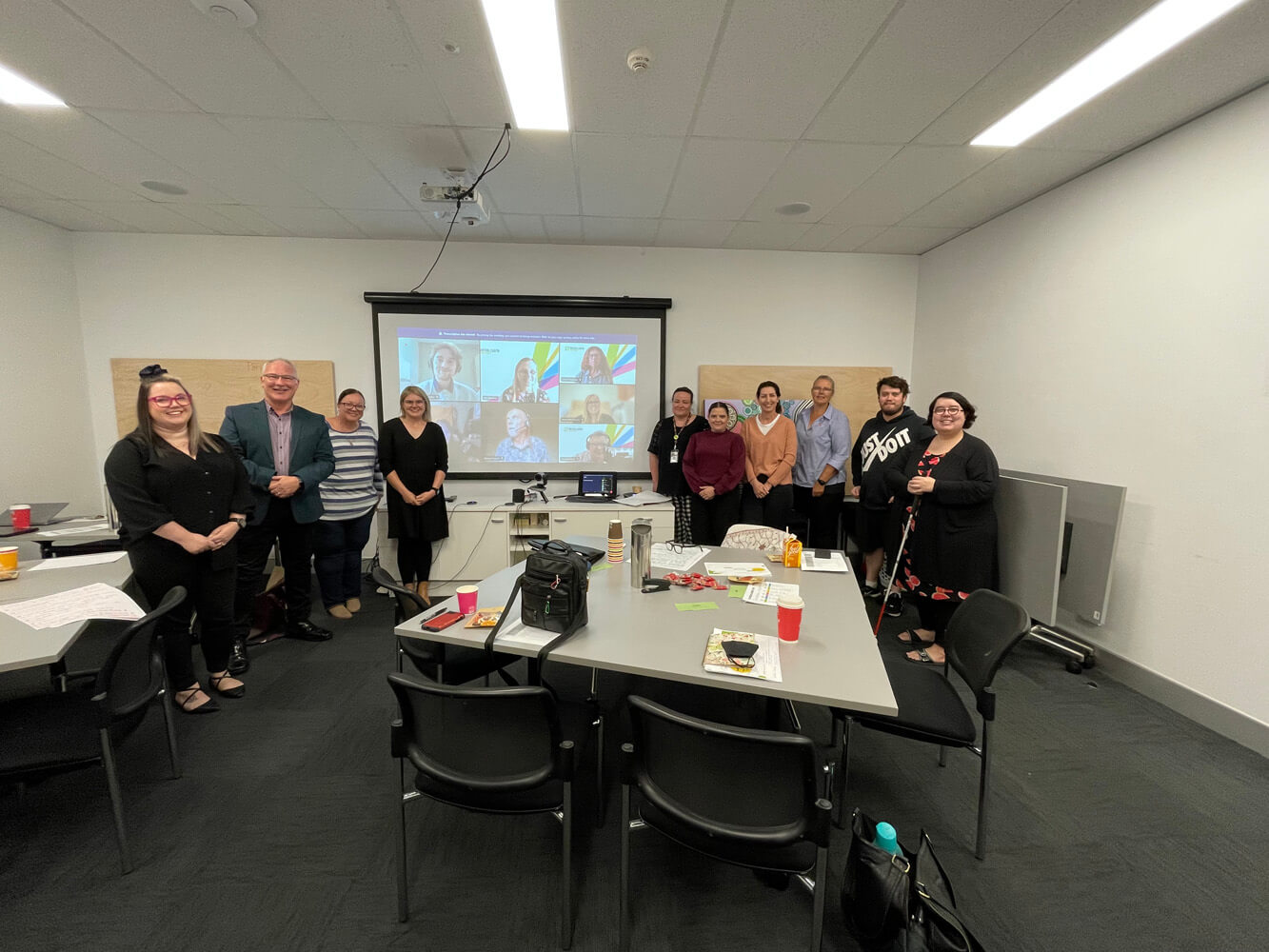 10 people standing in front of a screen with 7 more people who are attending via Zoom.