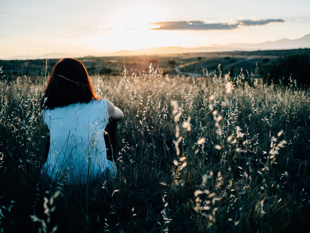 Young woman sitting by herself in a field with her back to the camera