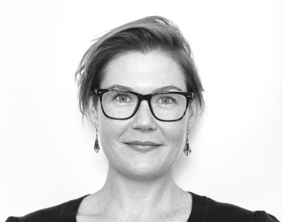 Woman with glasses and hair pinned up smiling at camera, in black and white