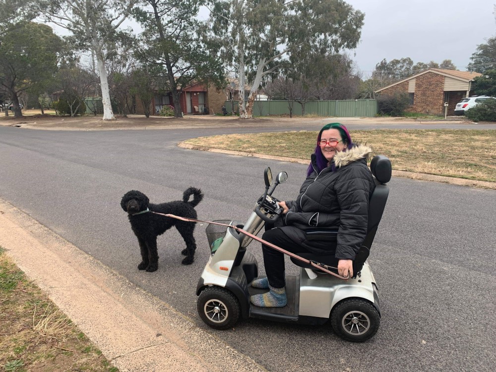 Woman in motorised scooter on road, walking a dog 