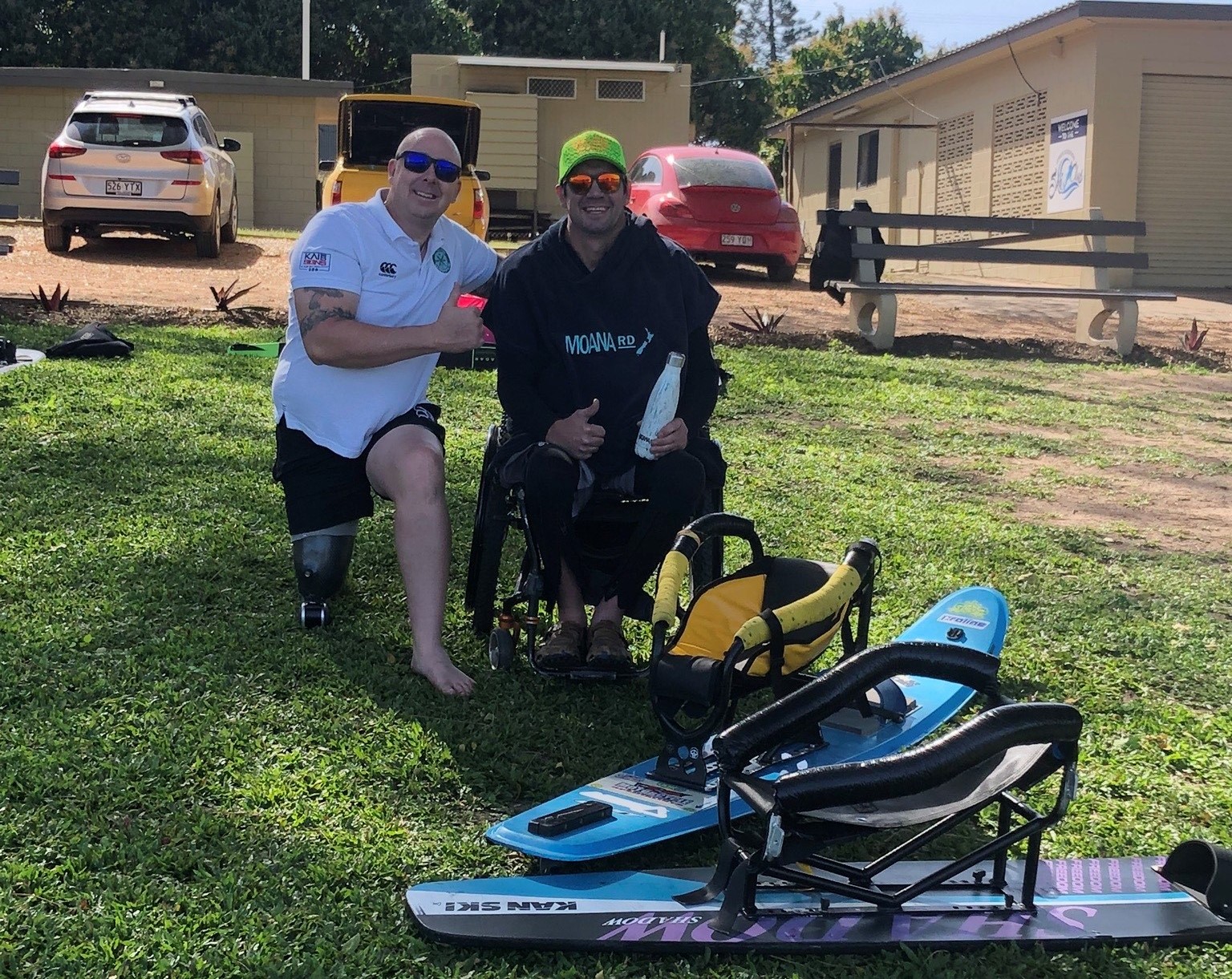 Two men with disability pose on grass with modified water skis