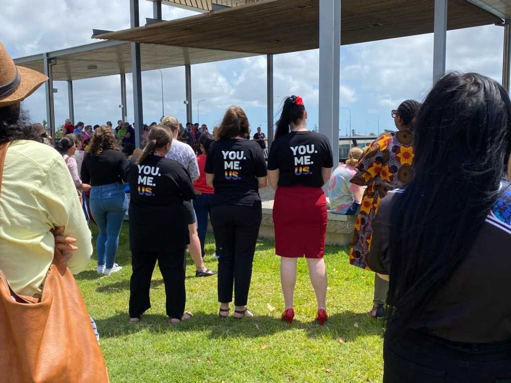 Three women with their backs to the camera wearing pride T-shirts that say 