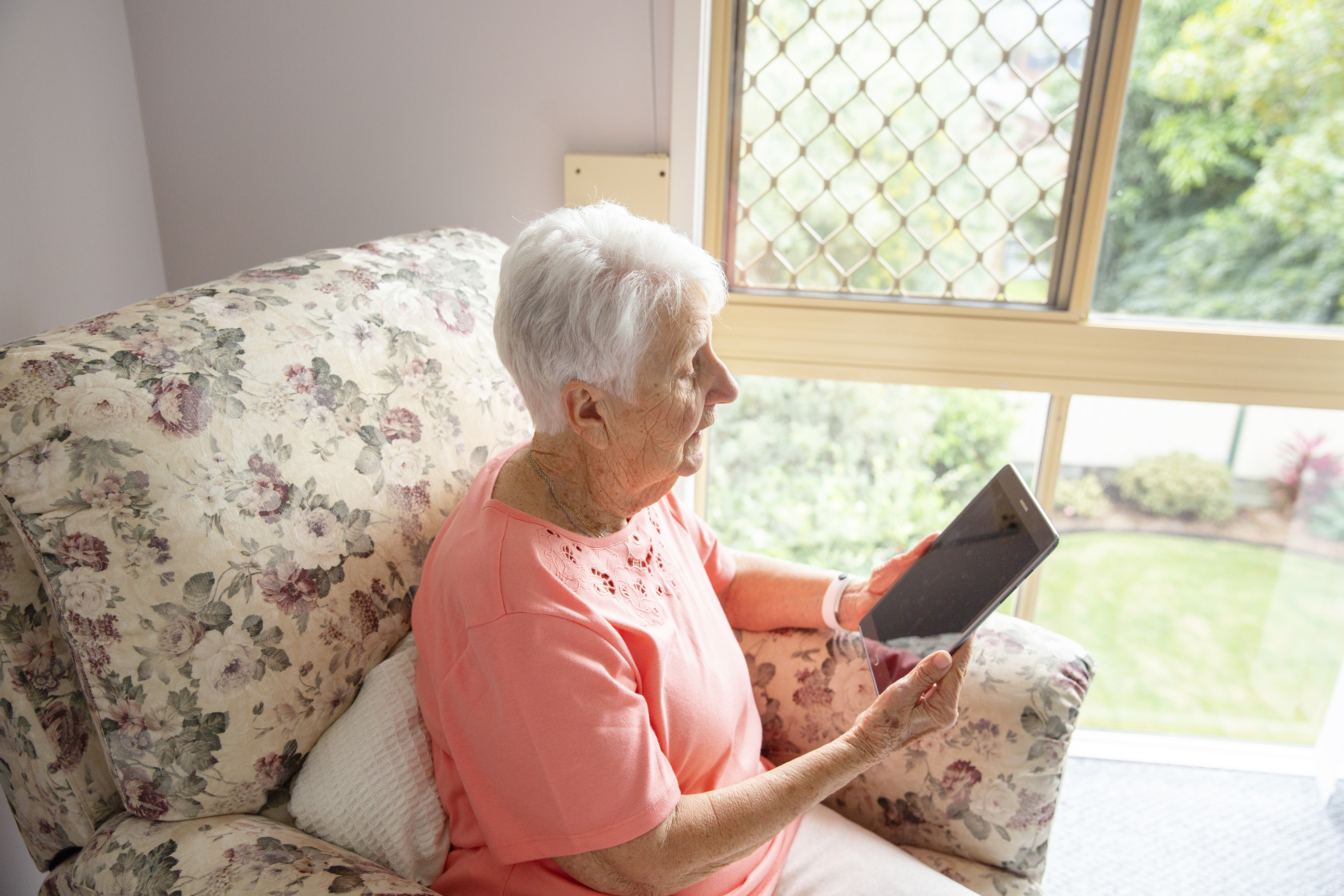 Senior lady sitting in armchair and looking at tablet in hand