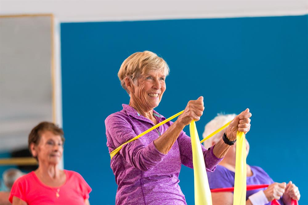 Senior lady smiling while holding yellow elastic band Senior lady smiling while holding yellow elastic band