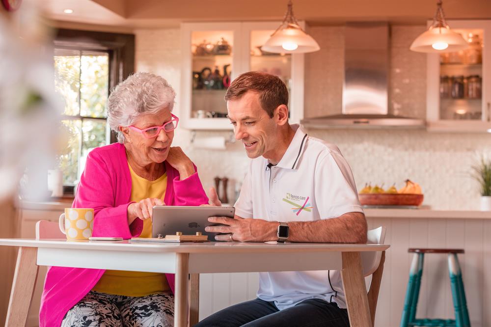 Lady with pink cardi on tablet with Feros Care man Lady with pink cardi on tablet with Feros Care man