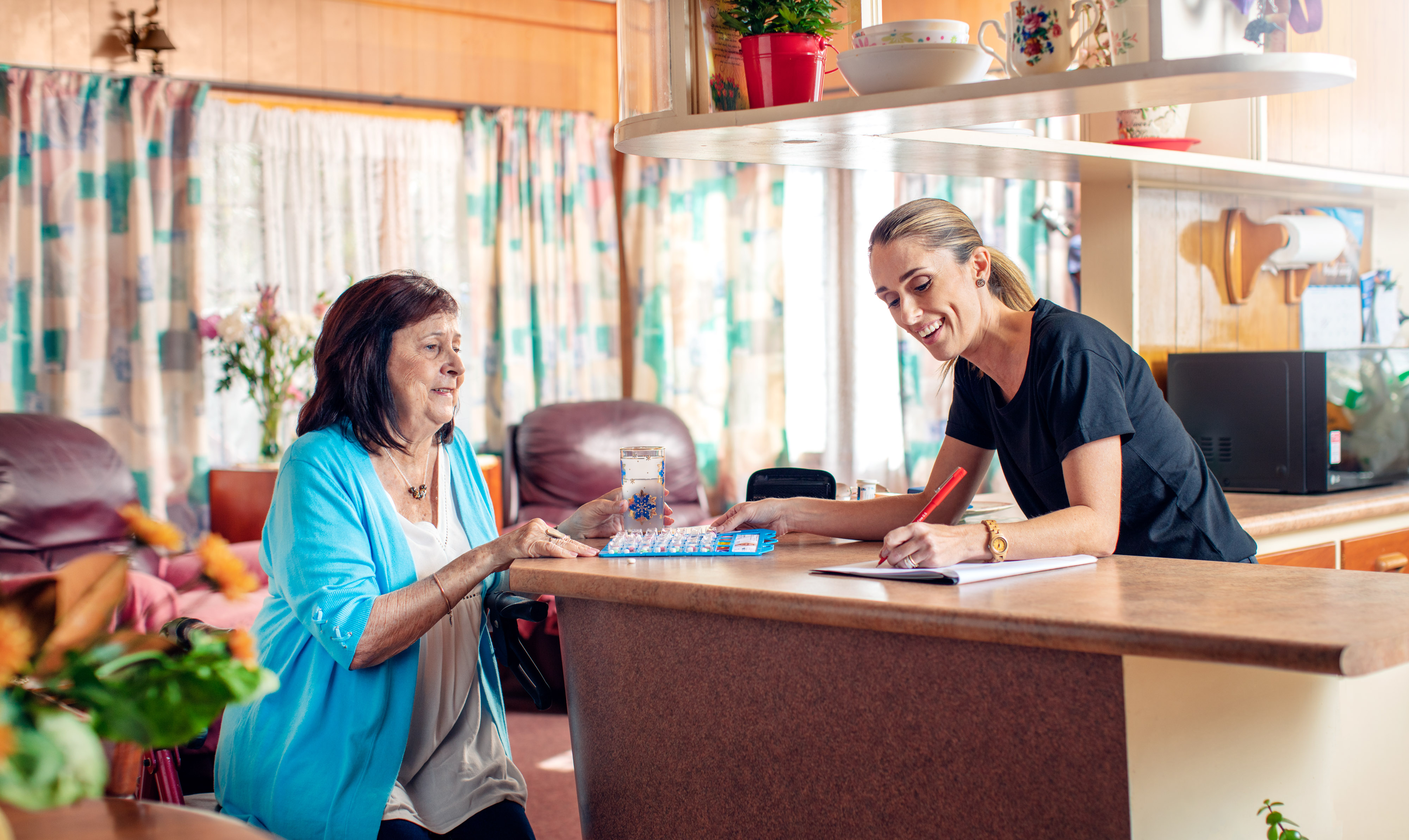 Aged care employee with senior lady in kitchen