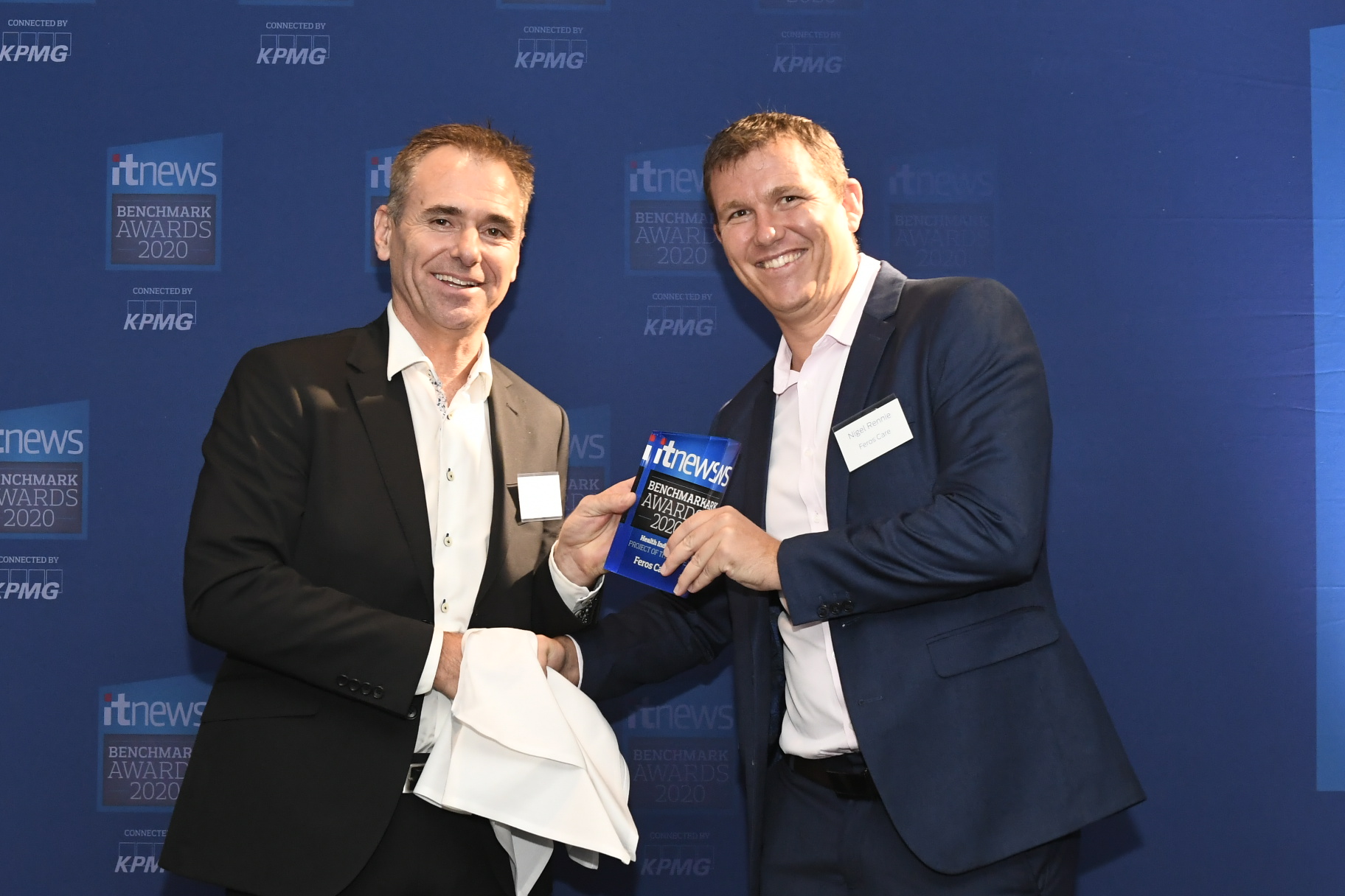 Two men shaking hands in front of IT news banner, one holding an award