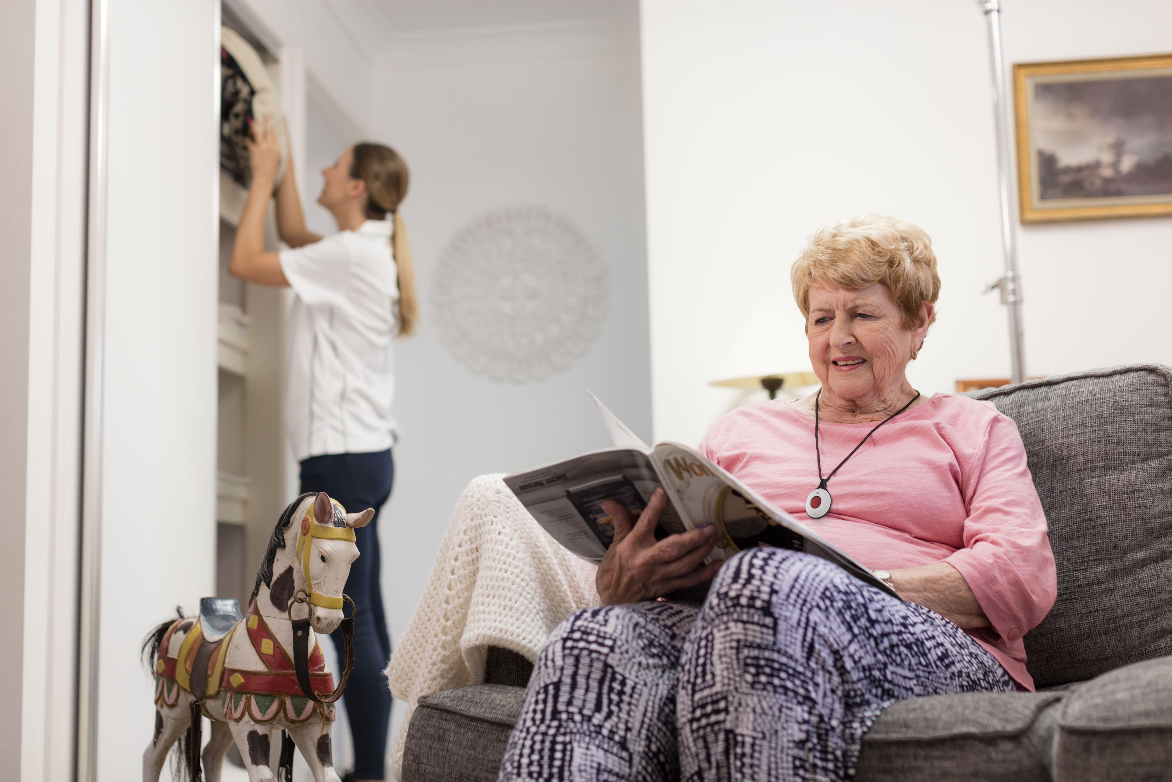 Senior lady sitting on couch with personal alarm pendant around neck