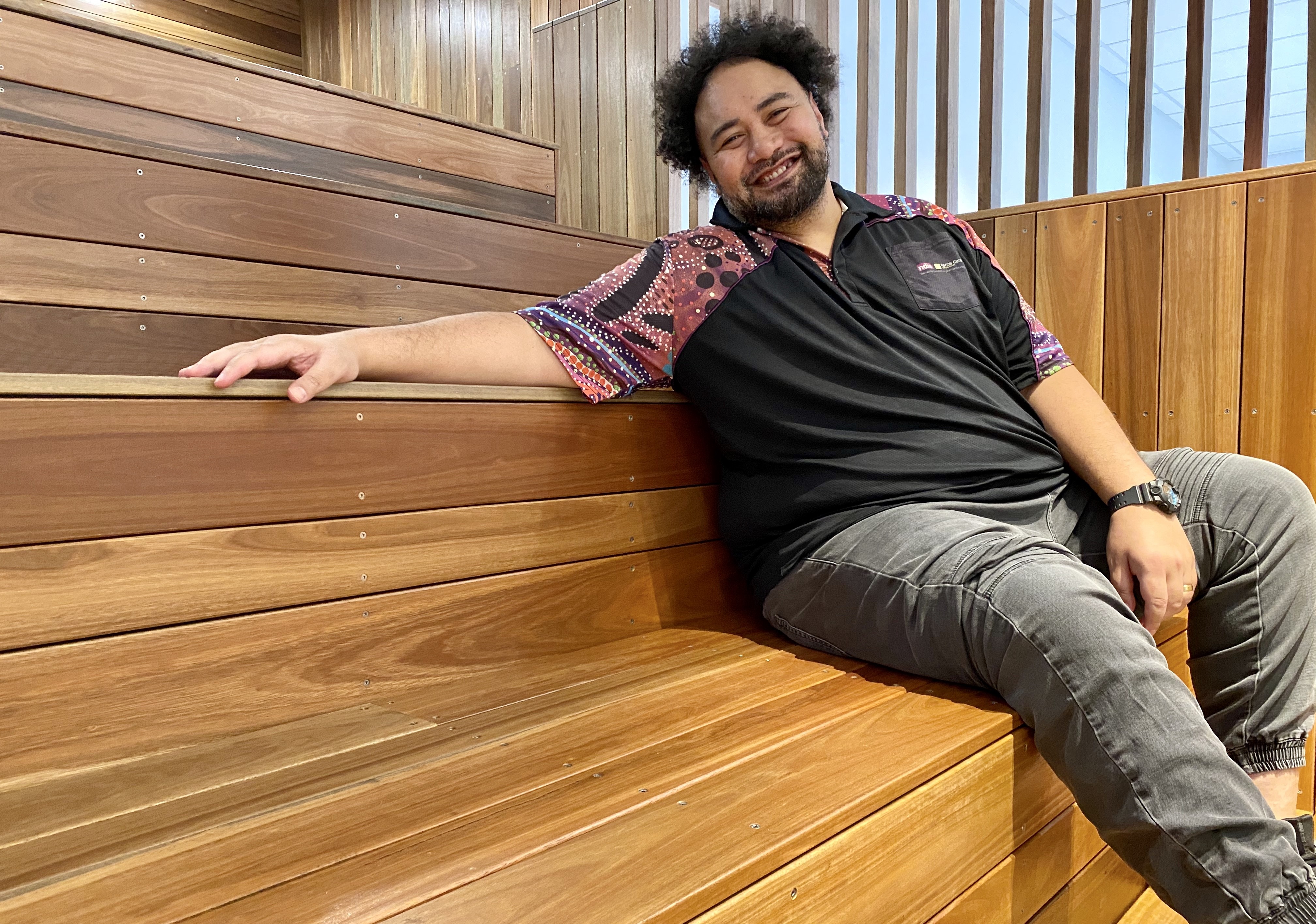 Man sitting on wooden stairs in Aboriginal T-shirt