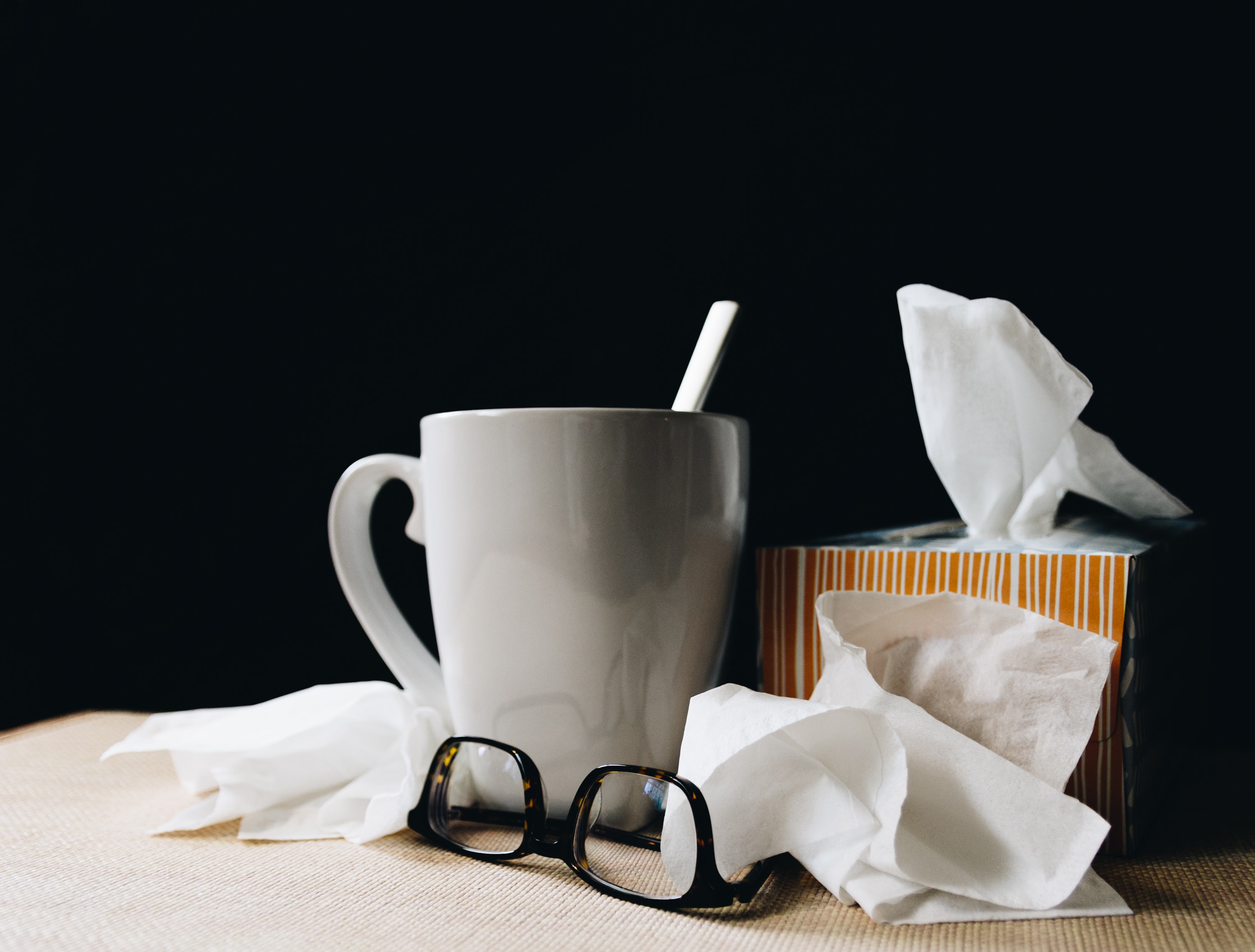 Mug, used tissues and a pair of glasses in front of a black background