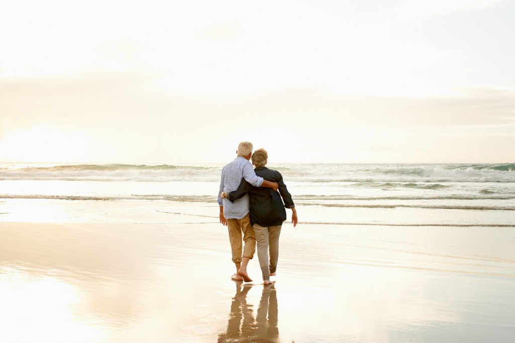 An elderly couple standing on the beach, hugging