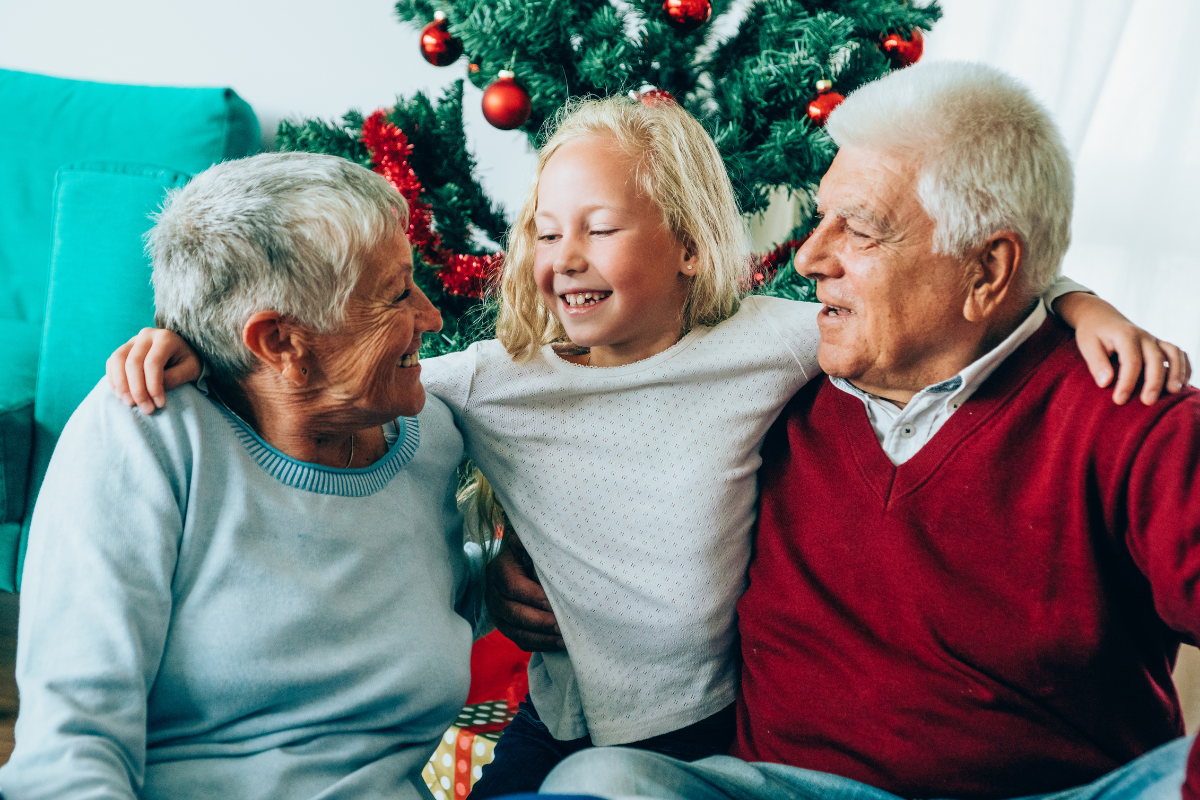 Senior woman and man being hugged by a young girl in front of a Christmas tree