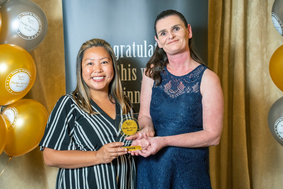 Two women holding a gold award in front of balloons