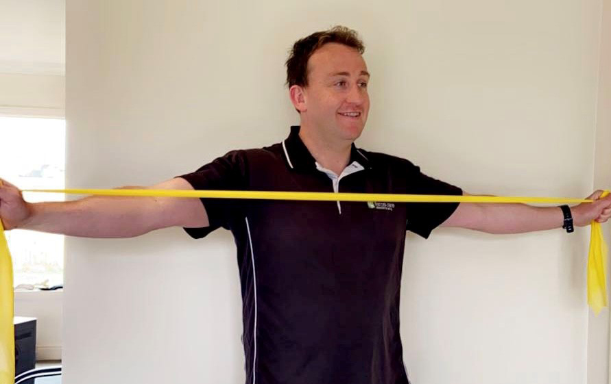 Photo of Josh, a Feros Care Exercise Physiologist, stretching out his arm with resistant band