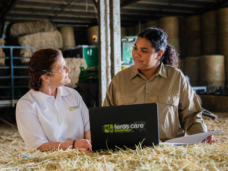 Local area coordinator talking with NDIS participant in a barn with laptop on top of a pile of hay.