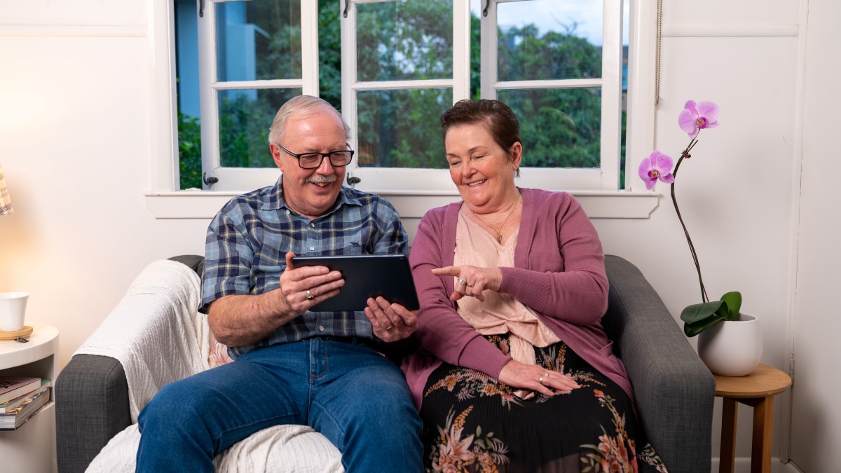 A senior lady and man looking at a tablet on a couch