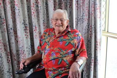 Senior man in Hawaiian shirt sitting in front of curtain