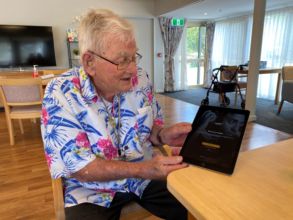 Senior man seated at table and holding an tablet with Audible open on it